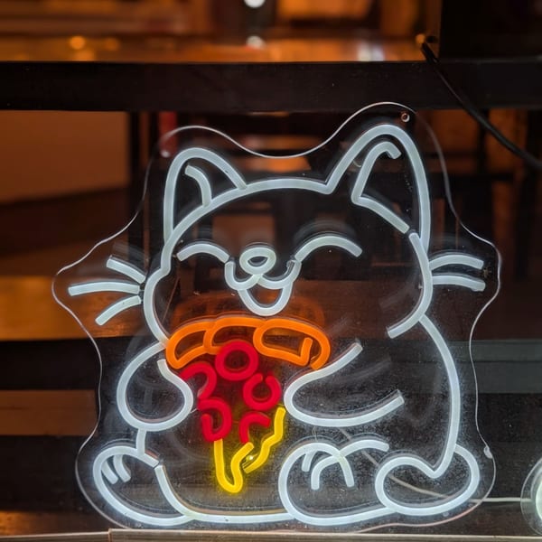A neon sign of a happy cat holding a slice of pizza, glowing white, red, orange, and yellow.