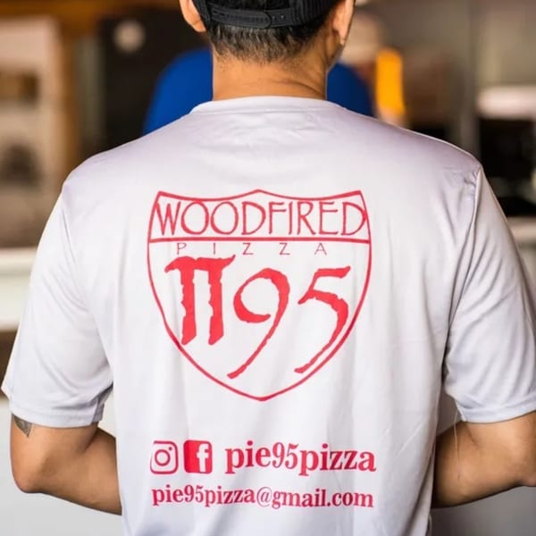 Back of a person wearing a white Pie95 Pizza shirt with a red logo and social media.