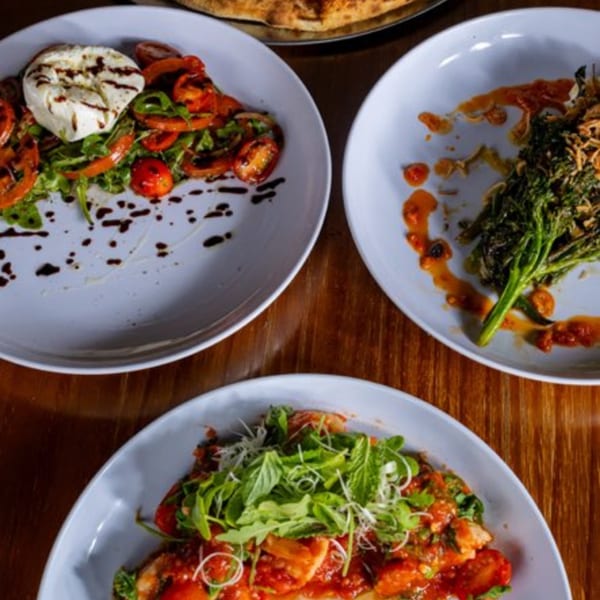 Three plates of Italian dishes, including a caprese salad, broccolini, and a pasta dish.