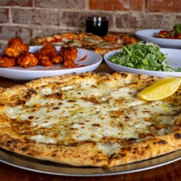 A white pizza with a lemon wedge, buffalo wings, salad, and another pizza on a brick background.
